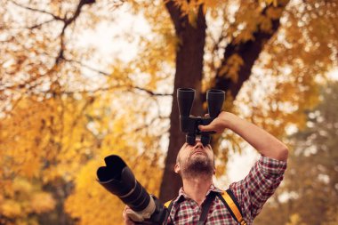 Dürbün ve kamera kullanan adam doğada kuşları ve hayvanları izliyor..