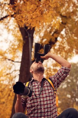 Dürbün ve kamera kullanan adam doğada kuşları ve hayvanları izliyor..