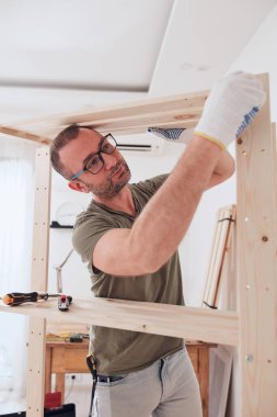 Yeni ahşap bir raf ve mobilya monte eden bir adam..