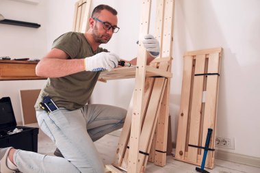 Yeni ahşap bir raf ve mobilya monte eden bir adam..