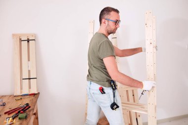 Yeni ahşap bir raf ve mobilya monte eden bir adam..