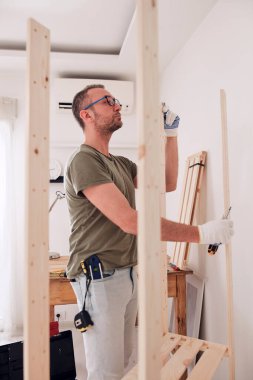 Yeni ahşap bir raf ve mobilya monte eden bir adam..