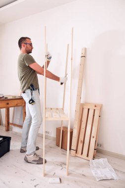 Yeni ahşap bir raf ve mobilya monte eden bir adam..