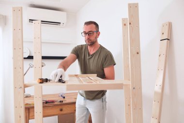 Yeni ahşap bir raf ve mobilya monte eden bir adam..