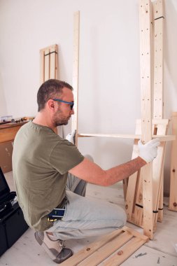 Yeni ahşap bir raf ve mobilya monte eden bir adam..