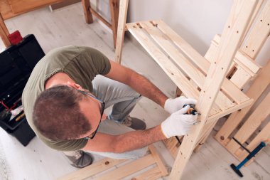 Yeni ahşap bir raf ve mobilya monte eden bir adam..