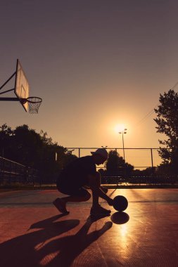 Altın saatinde halka açık bir sahada basketbol topu olan bir adam..