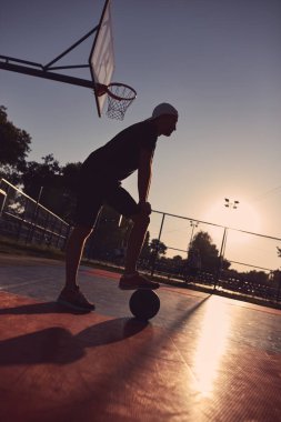 Altın saatinde halka açık bir sahada basketbol topu olan bir adam..