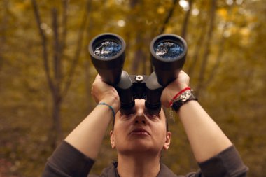 Woman using binoculars for birdwatching and observing other animals in nature. clipart