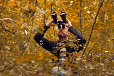 Dürbün ve kamera kullanan bir adam kuşları ve doğadaki diğer gözlemci hayvanları izliyor..