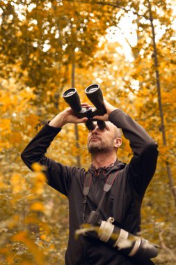 Dürbün ve kamera kullanan bir adam kuşları ve doğadaki diğer gözlemci hayvanları izliyor..