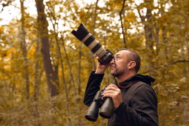 Dürbün ve kamera kullanan bir adam kuşları ve doğadaki diğer gözlemci hayvanları izliyor..