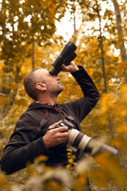 Dürbün ve kamera kullanan bir adam kuşları ve doğadaki diğer gözlemci hayvanları izliyor..