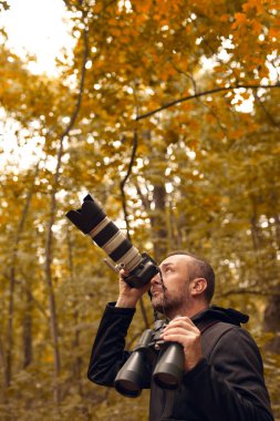 Dürbün ve kamera kullanan bir adam kuşları ve doğadaki diğer gözlemci hayvanları izliyor..