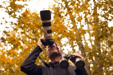 Dürbün ve kamera kullanan bir adam kuşları ve doğadaki diğer gözlemci hayvanları izliyor..