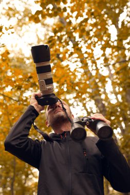 Dürbün ve kamera kullanan bir adam kuşları ve doğadaki diğer gözlemci hayvanları izliyor..
