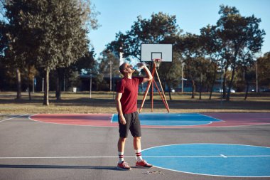 Adam şehir parkında halka açık bir basket sahasında egzersiz yapıyor ve esniyor..