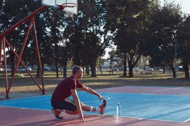Adam şehir parkında halka açık bir basket sahasında egzersiz yapıyor ve esniyor..