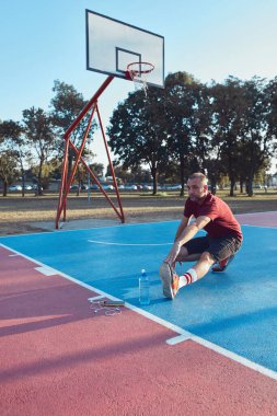 Adam şehir parkında halka açık bir basket sahasında egzersiz yapıyor ve esniyor..