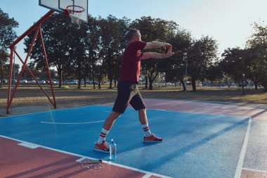 Adam şehir parkında halka açık bir basket sahasında egzersiz yapıyor ve esniyor..