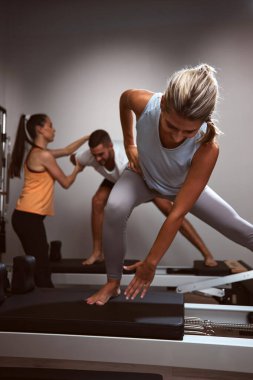 Genç bir kadın ve erkek spor salonunda pilates makinesinde kişisel antrenörleriyle egzersiz yapıyorlar..