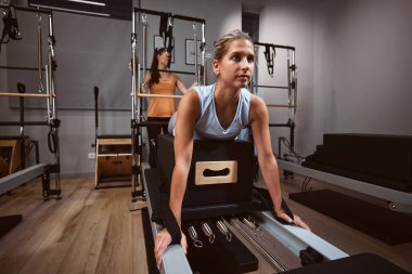 Genç bir kadın spor salonunda kişisel antrenörüyle pilates makinesinde egzersiz yapıyor..