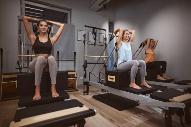 Genç kadınlar spor salonunda pilates makinesinde kişisel antrenörleriyle egzersiz yapıyorlar..