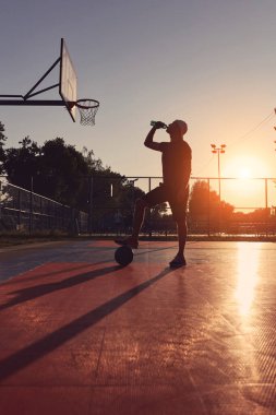 Adam halka açık basketbol sahasında su içiyor..