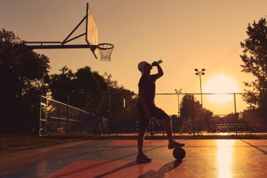 Adam halka açık basketbol sahasında su içiyor..