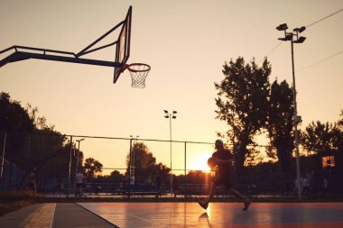 Adam halka açık bir sahada basketbol oynuyor..