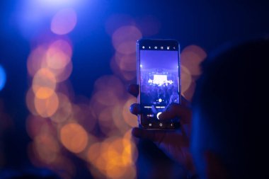Elinde sahne ışıkları olan konser kalabalığının arka plan siluetleri olan akıllı telefon tutan kişi