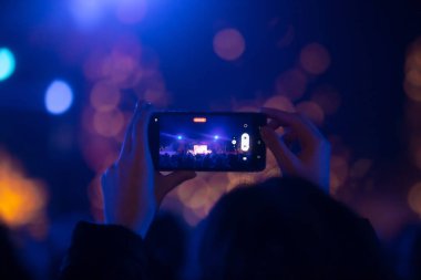 Elinde sahne ışıkları olan konser kalabalığının arka plan siluetleri olan akıllı telefon tutan kişi