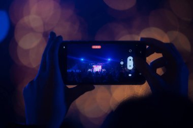 Elinde sahne ışıkları olan konser kalabalığının arka plan siluetleri olan akıllı telefon tutan kişi