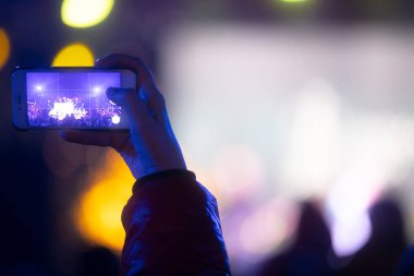 Elinde sahne ışıkları olan konser kalabalığının arka plan siluetleri olan akıllı telefon tutan kişi