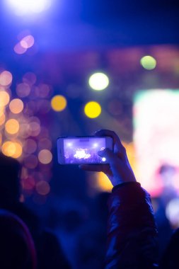 Elinde sahne ışıkları olan konser kalabalığının arka plan siluetleri olan akıllı telefon tutan kişi