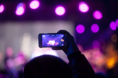 Elinde sahne ışıkları olan konser kalabalığının arka plan siluetleri olan akıllı telefon tutan kişi