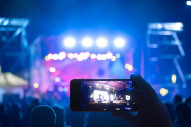 Elinde sahne ışıkları olan konser kalabalığının arka plan siluetleri olan akıllı telefon tutan kişi
