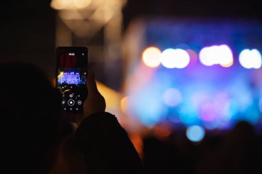 Elinde sahne ışıkları olan konser kalabalığının arka plan siluetleri olan akıllı telefon tutan kişi