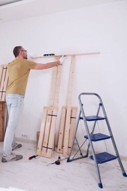 Yeni ahşap bir raf ve mobilya monte eden bir adam..