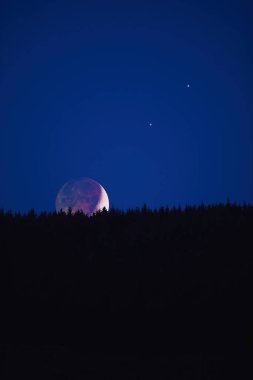 Balmumu ay, gezegenler ve yıldızlar dağ siluetlerinin arkasında yükseliyor..