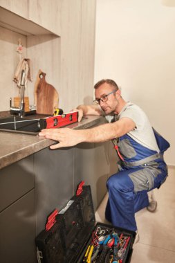 Mutfak lavabosundaki musluğu tamir edip onarıyor..