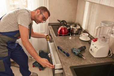 Tamirci dairedeki mutfak dolaplarını tamir ediyor..