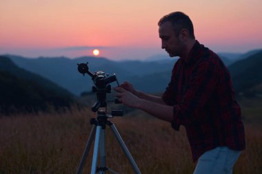 Astronom bir teleskopla güneşe bakıyor ve cep telefonu kullanıyor..