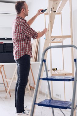 Yeni ahşap bir raf ve mobilya monte eden bir adam..