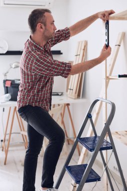 Yeni ahşap bir raf ve mobilya monte eden bir adam..