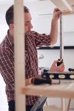 Yeni ahşap bir raf ve mobilya monte eden bir adam..