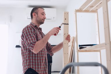 Yeni ahşap bir raf ve mobilya monte eden bir adam..