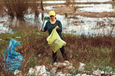 Gönüllü ve çevreci eylemci çöplerle dolu kirli göl kıyılarını temizliyor..