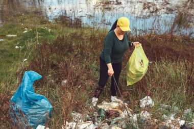 Gönüllü ve çevreci eylemci çöplerle dolu kirli göl kıyılarını temizliyor..