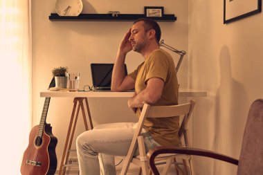 Evde dizüstü bilgisayarla çalışırken karın ağrısı ve baş ağrısı çeken bir adam..